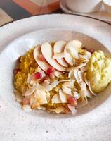 Nutritious millet porridge topped with fresh apple slices, pomegranate seeds, and coconut flakes, served with a creamy side. An appealing and healthy gluten free breakfast option photo