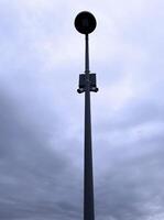 Streetlight against grey, overcast sky. The tall lamp post is central in the image, with a cloudy background, emphasizing urban infrastructure and atmospheric conditions photo