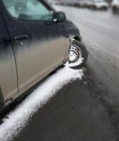 Close-up image of a car with a detached front wheel, stuck in snowy and icy road conditions. Visible damage to the vehicle emphasizes road safety challenges during winter photo