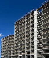 High-rise building under construction with exposed concrete framework and wooden scaffolding under a clear blue sky background, modern urban development progress photo
