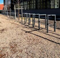 Empty metal bike racks lined up on gravel path outside a modern building, casting distinct shadows on the ground in quiet urban setting copy space photo