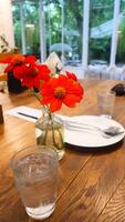 A flower vase, glass of water, plate, spoon, and fork are beautifully arranged on a wooden table in a cafe photo