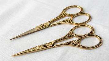 Two gold scissors sitting on a white cloth photo