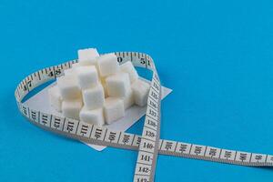 Sugar cubes arranged in heart shape with measuring tape on blue background photo