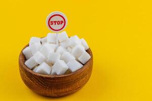 Bowl filled with sugar cubes and a stop sign on a bright yellow background photo