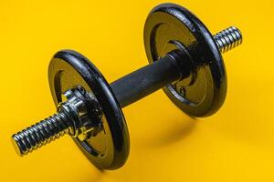 Black dumbbell on vibrant yellow background for fitness photo
