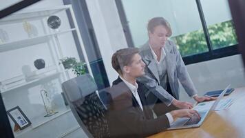 Business professionals collaborate in a modern office setting while analyzing data on a laptop video