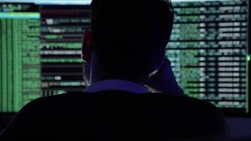 nel un' buio camera illuminato di blu luce, un' giovane uomo si concentra intensamente su codifica compiti. Due grande monitor Schermo flussi di codice e dati come lui naviga attraverso programmazione sfide video