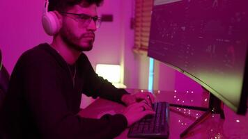 Data analyst working on computer setup with dual monitors in a colorful ambient light at home studio during evening video