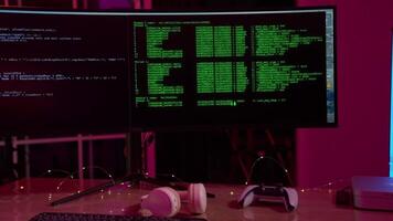 In a well-lit workspace, two monitors showcase lines of green code and programming data, while gaming headphones and a controller rest on the desk, indicating a blend of work and play. video