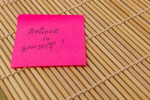 Positive affirmation note on pink sticky paper resting on bamboo mat photo