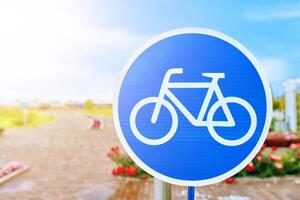 A vibrant blue and white sign showcasing a bicycle wheel against the azure sky and fluffy clouds, symbolizing nature and freedom. The design includes bicycle handlebars and frame details photo