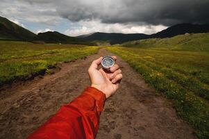 Man explorer searches for direction with a compass in a green field on an off-road. A first-person view of the upcoming path through the mountains photo