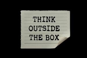 Think outside the box message written on ripped torn paper piece on black background. Conceptual think outside the box symbol. Copy space. photo