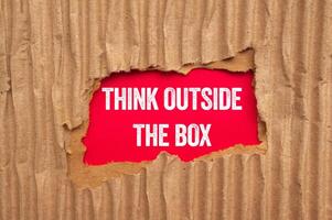 Think outside the box message written on ripped torn cardboard paper on red background. Conceptual think outside the box symbol. Copy space. photo