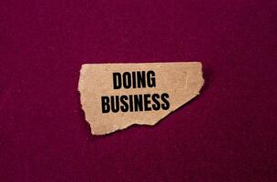 Doing business message written on ripped torn brown paper piece on purple background. Conceptual doing business symbol. Copy space. photo