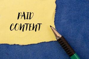 Paid content message written on ripped torn yellow paper on blue background. Conceptual paid content symbol. Copy space. photo