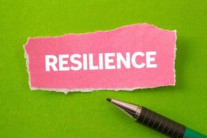 Resilience message written on ripped torn pink paper piece on green background. Conceptual resilience symbol. Copy space. photo