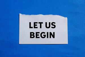 Let us begin message written on ripped torn white paper piece on blue background. Conceptual let us begin symbol. Copy space. photo