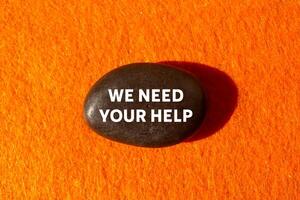 We need your help message written on black stone on orange background. Conceptual we need your help symbol. Copy space. photo