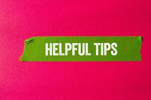 Helpful tips message written on ripped torn green paper tape on pink background. Conceptual helpful tips symbol. Copy space. photo