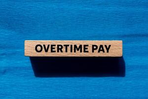 Overtime pay message written on wooden block on blue background. Conceptual overtime pay symbol. Copy space. photo
