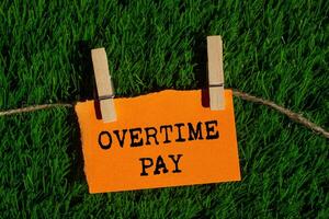 Overtime pay message written on ripped torn orange paper piece on green grass background. Conceptual overtime pay symbol. Copy space. photo
