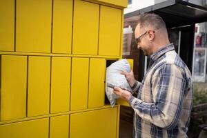 Man retrieving package from yellow delivery locker in a city setting during daylight hours photo