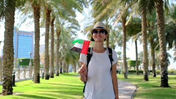 Woman tourist holding small UAE flag against Corniche Walking Trail in Abu Dhabi. Blend of nature, patriotism, and serenity, with lush greenery , views symbolizing harmony progress. video