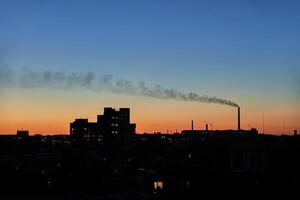 City skyline and factory at sunset with smoke plume against colorful evening sky. photo