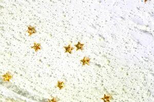 Golden star confetti on white frosted surface with glittering details and textured background. photo