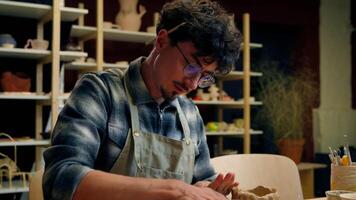 Concentrated man potter sculptor craftsman male Caucasian guy designer artist master in pottery workshop process modeling clay with rolling pin on table professional tool handmade craft ceramics hobby video