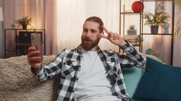 Young man blogger at home, sofa selfie mode, waving to camera, fun story, casual influencer vibe video