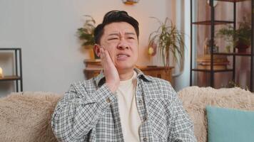 Young man touching cheek with expression of terrible suffer from painful toothache on sofa at home video
