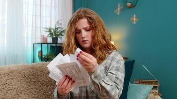 Woman sits on sofa holding bills and receipts worried with head in hands stressed by money problems video
