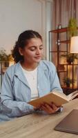 indiano jovem mulher lendo livro girando Páginas sorridente desfrutando literatura levando descansar senta às mesa video