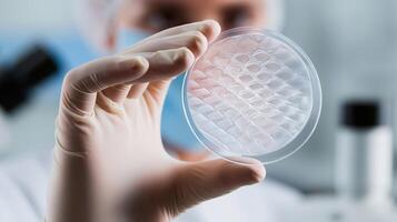 A scientist in protective gear examines an artificial skin sample in a petri dish. The biopolymer structure represents advancements in regenerative medicine, wound healing, and tissue engineering. photo