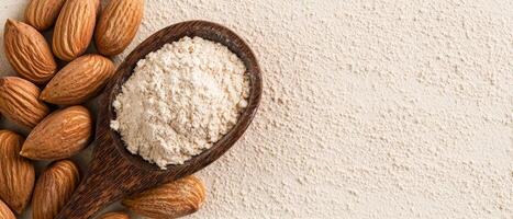A wooden spoon holds almond flour next to whole almonds on a textured surface, highlighting a healthy ingredient for cooking and baking. photo