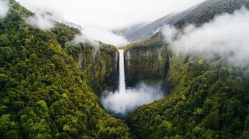 A stunning waterfall cascades into a lush, green valley, surrounded by misty mountains and dense forests, creating a serene natural landscape. photo