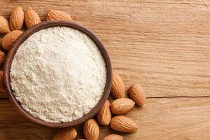 A wooden bowl filled with almond flour surrounded by whole almonds on a rustic wooden surface. photo