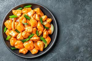 A delicious plate of orange chicken, garnished with green onions, against a dark textured background, highlighting its vibrant colors and appetizing appeal. photo