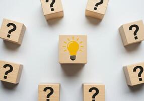 Wooden Block with Lightbulb Surrounded by Question Marks Representing New Ideas and Solutions photo