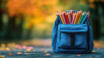 Bright colored pencils in a blue backpack resting on a path lined with autumn leaves photo