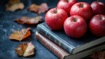 Fresh red apples on old books with autumn leaves arranged on a dark background, creating a cozy seasonal display photo