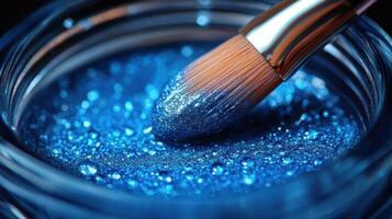 Close-up view of a makeup brush dipped in shimmering blue cosmetic glitter in a glass jar photo