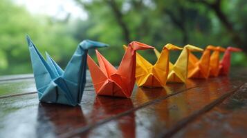 Colorful origami cranes lined up on a wooden table set against a lush green background during a rainy day photo