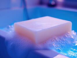 Bar of creamy white soap with luscious foam and bubbles, resting on the edge of a bathtub. Soft lighting with a gentle blue hue, creating a calm and soothing effect photo