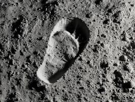 Single shoe print impression in fine granular surface, resembling extraterrestrial ground, surrounded by small rocks and uneven texture, captured with high contrast grayscale photo