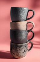 Stacked Black and Gray Mugs with One Handle on Pink Background photo