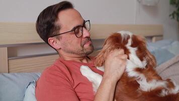 a man relaxes on his bed, stroking his dog affectionately in a warm and inviting space. their bond is evident as he gazes happily . concept for pet care, veterinary services, animal companionship. video